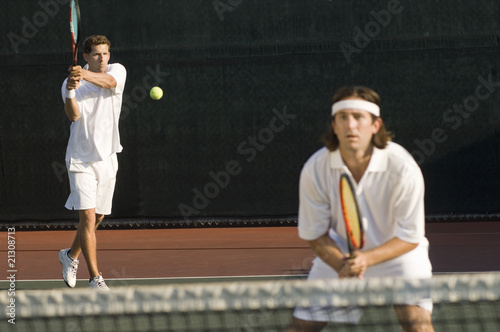 tennis player hitting backhand; doubles partner squatting at net