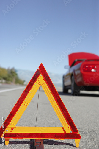 warning triangle in front of broken down red sports car at side of road