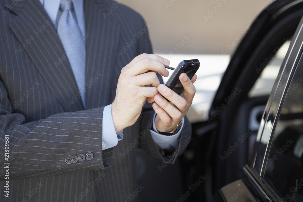 businessman using pda beside car mid section businessman using pda beside car mid section