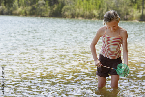 Fototapeta Naklejka Na Ścianę i Meble -  girl (7-9) standing knee-deep in lake holding fishing net.