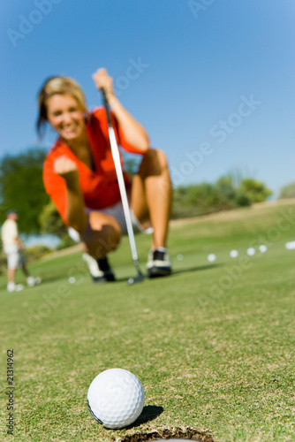 female golfer looking at ball rolling towards cup focus on ball