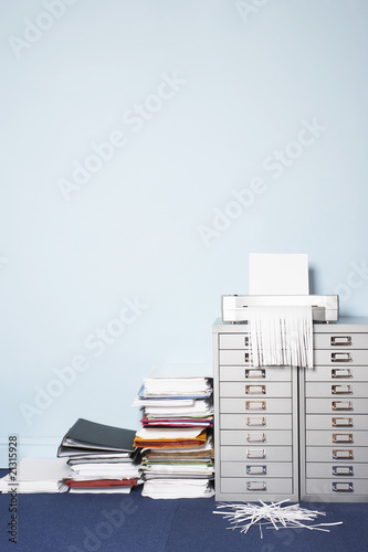 shredder on file cabinet stack of paperwork on floor in office