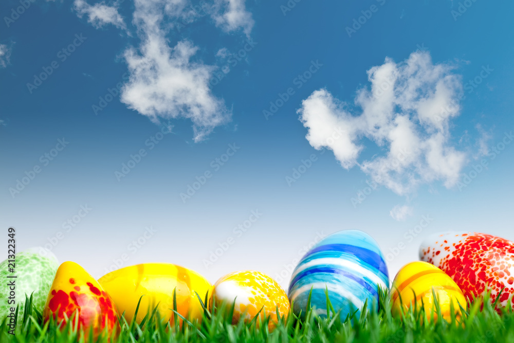 Easter eggs in green grass over blue sky with clouds Easter eggs in green grass over blue sky with clouds