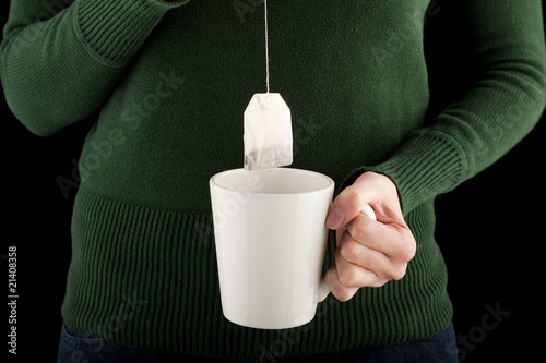 female hands holding a teacup and teabag