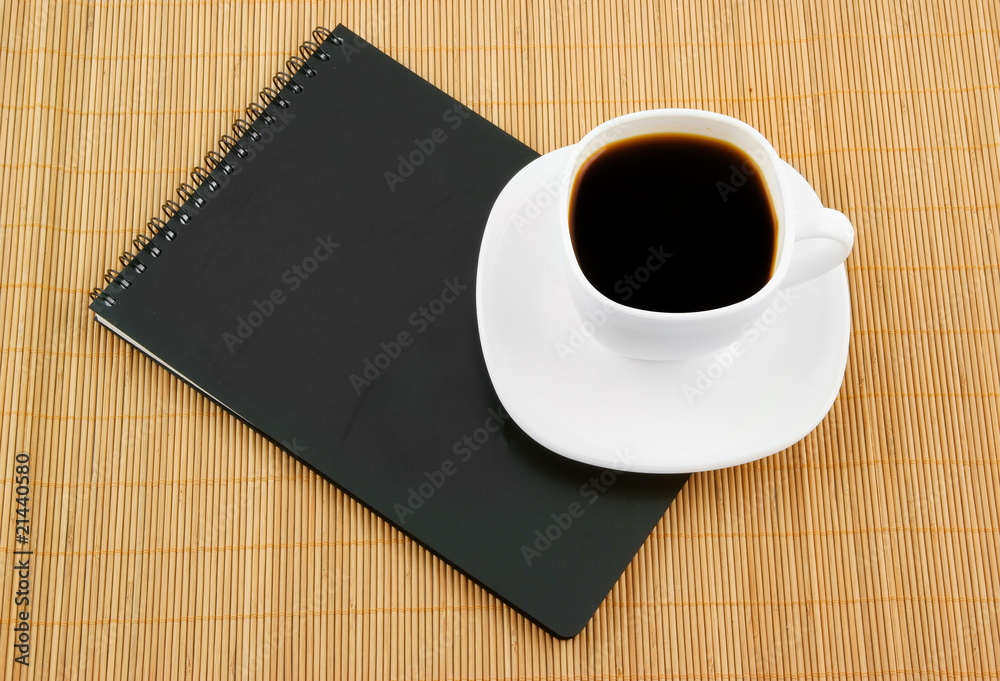 Black spiral squared notebook with cup of coffee