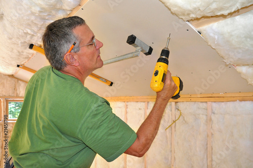 Man using cordless drill to attach drywall panel to ceiling