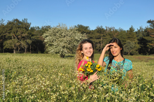 Two beautiful young women standing in blooming meadow