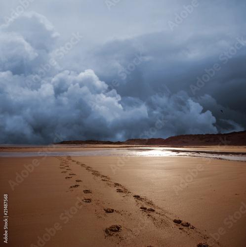 Dark storm shown behind prints on a beach