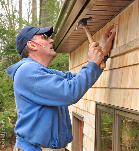 Carpenter nailing cedar shingles to exterior wall