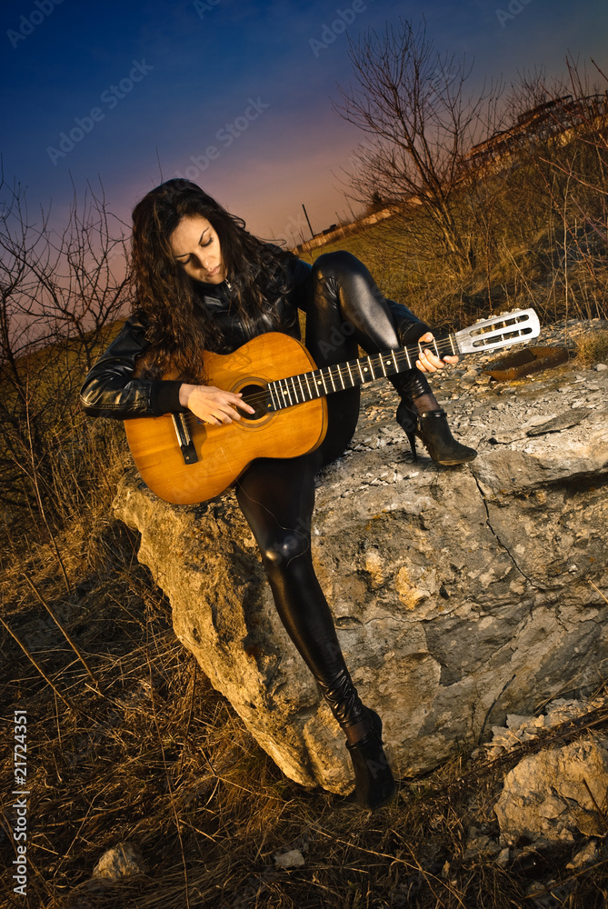 young woman play guitat at sunset rock