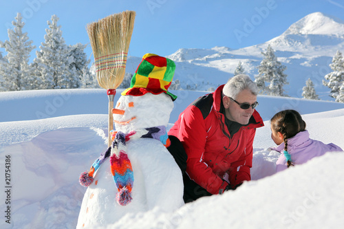 Homme senior et fillette près d'un bonhomme de neige