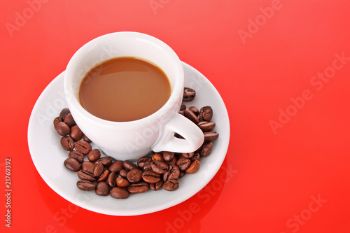 Small white cup of coffee with coffee grain on red background