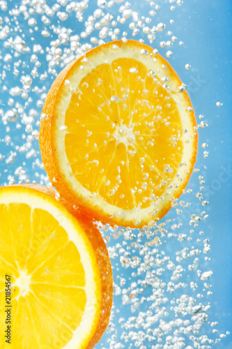 Fresh orange dropped into water with bubbles.