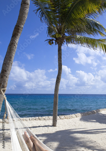 Female leg in hammock on background of ocean and sky..