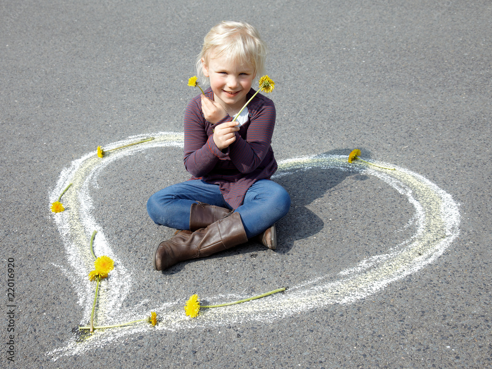Naklejka premium Little girl sitting in a white heart playing with flowers