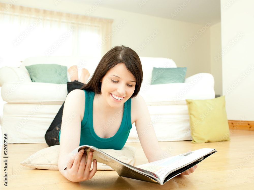 Smiling woman reading a magazine lying down on the floor Smiling woman reading a magazine lying down on the floor