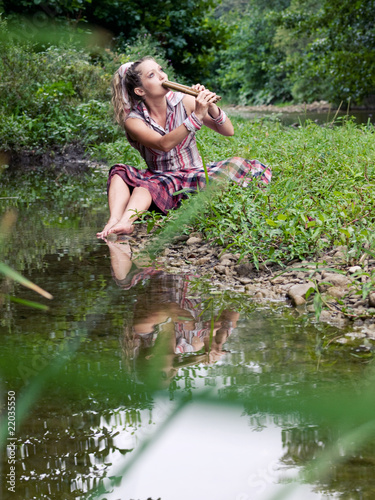 Fototapeta Naklejka Na Ścianę i Meble -  beautiful young girl with fife playing near river