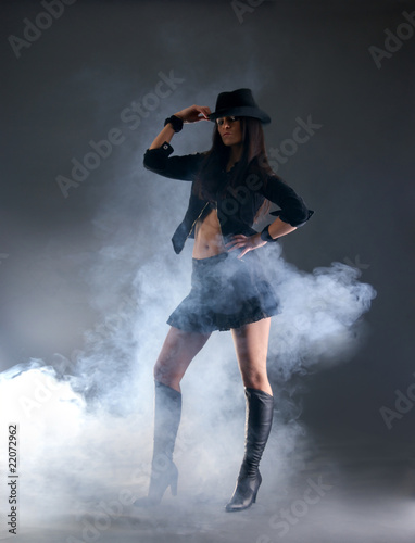 Sexy woman in a black hat posing on a foggy background