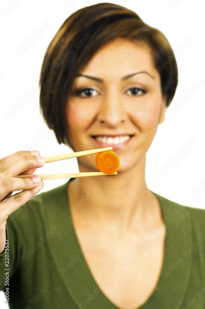 Young woman holds a carrot slice with chopsticks in front of her Young woman holds a carrot slice with chopsticks in front of her