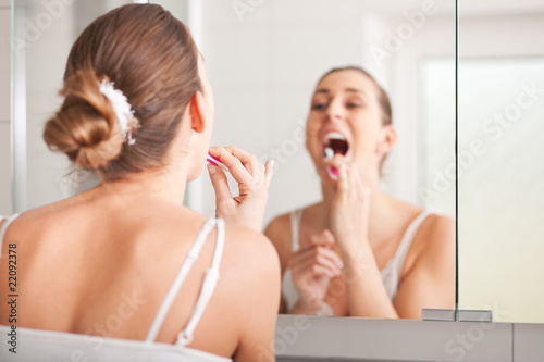 Junge Frau putzt sich die Zähne vor dem Spiegel