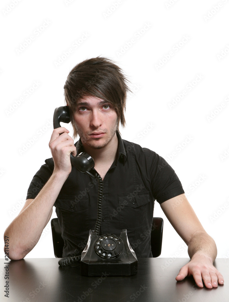 Handsome young guy in black t-shirt sitting frontally at a table with an old black telephone.