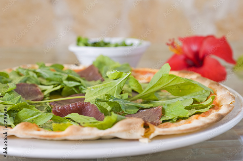 Meat pizza on a thin base with green salad topping