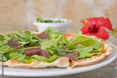 Meat pizza on a thin base with green salad topping