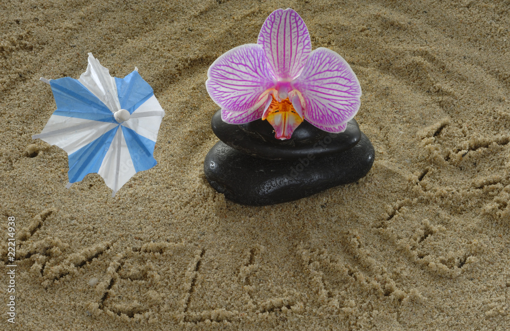 Fototapeta premium Steine mit Orchidee und Sonnenschirmchen auf Sand