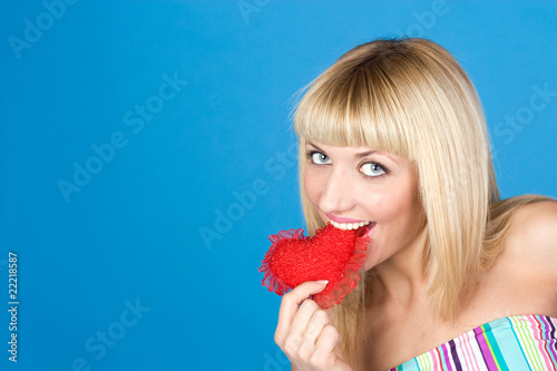 Attractive woman biting a red heart over blue background © Karyna Chekaryova