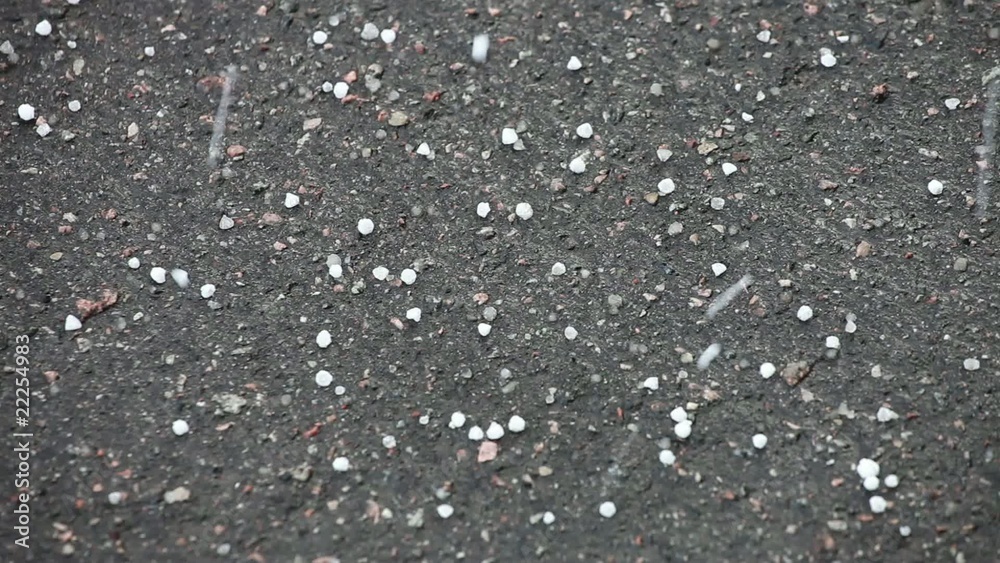 White hailstones bouncing off black asphalt during a hail storm