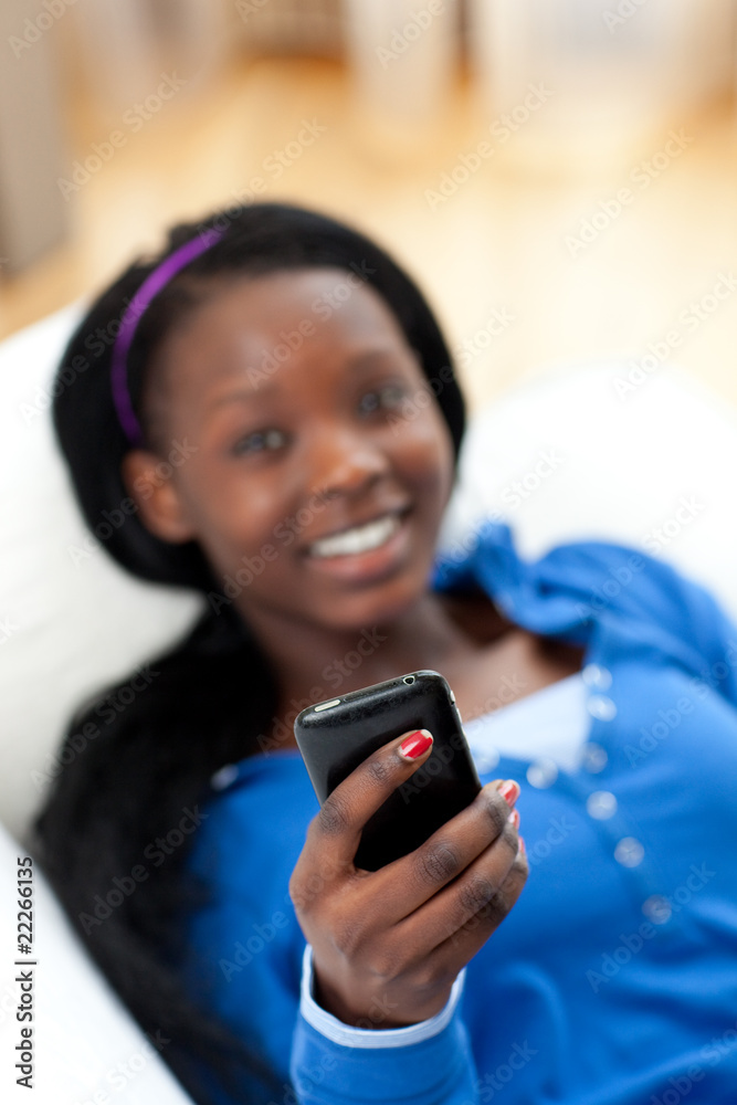 Fototapeta premium Afro-American woman sending a text lying on a sofa