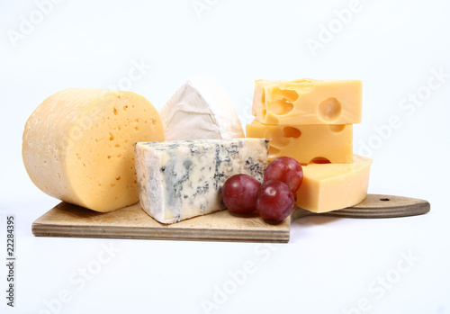 Various types of cheese and some red grapes on white
