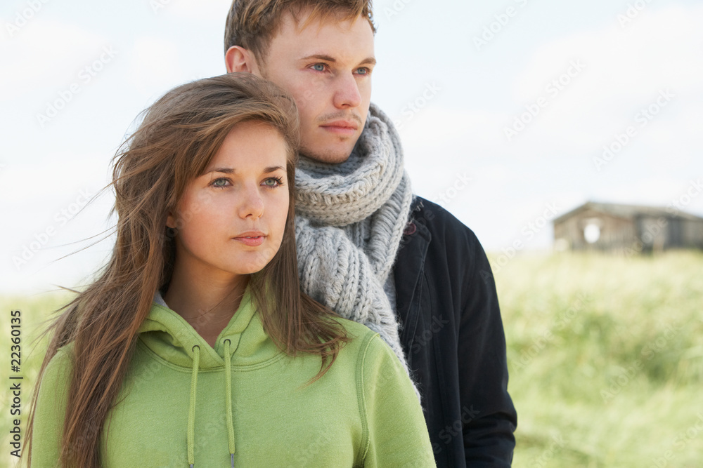 Obraz premium Romantic Young Couple Standing By Dunes With Beach Hut In Distan
