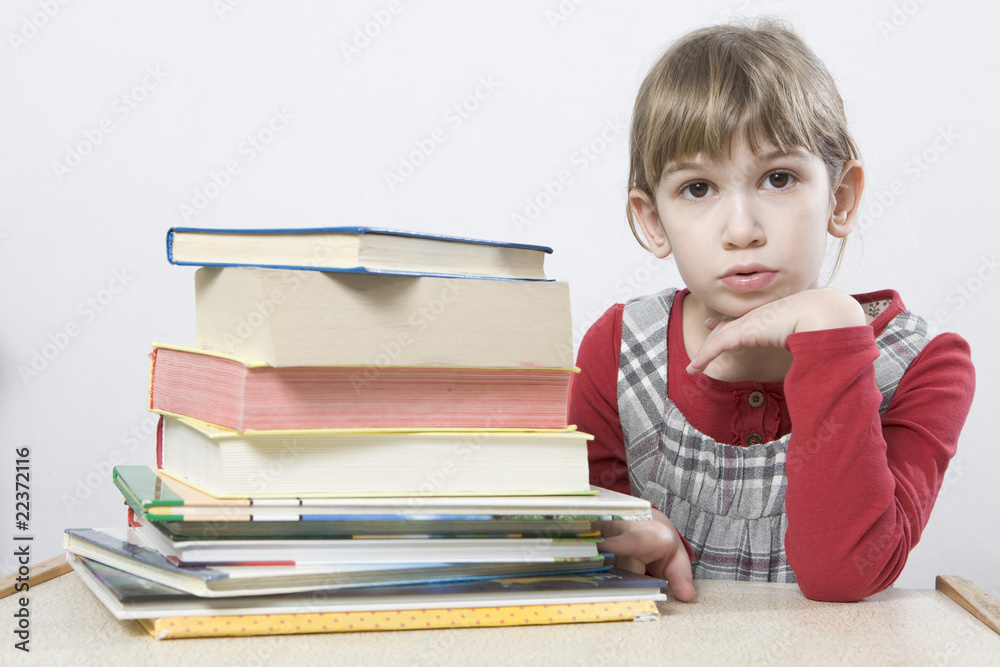 little cute sad girl with a pile of book sitting at table. little cute sad girl with a pile of book sitting at table.