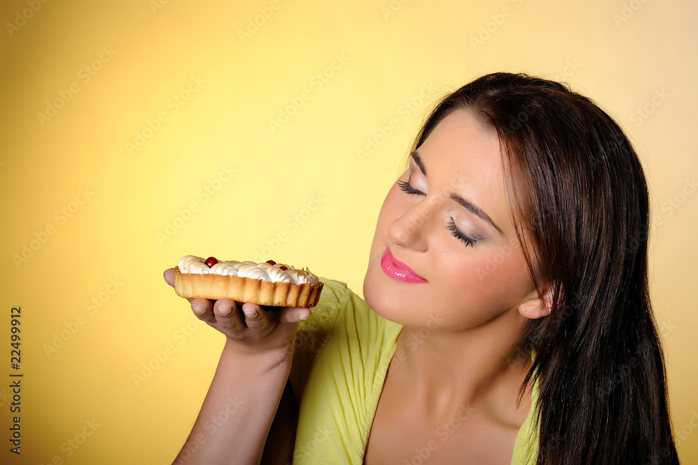 young beautiful girl eating small sweet cake. yellow background young beautiful girl eating small sweet cake. yellow background