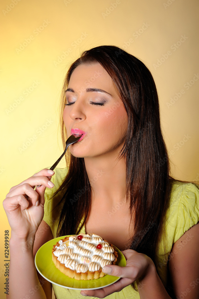 young beautiful girl eating small sweet cake. yellow background young beautiful girl eating small sweet cake. yellow background
