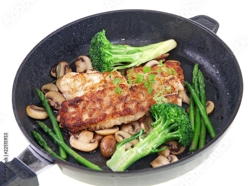 fried fish with vegetables in a black pan isolated on white