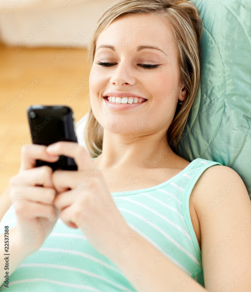 Smiling young woman sending a text lying on a sofa Smiling young woman sending a text lying on a sofa