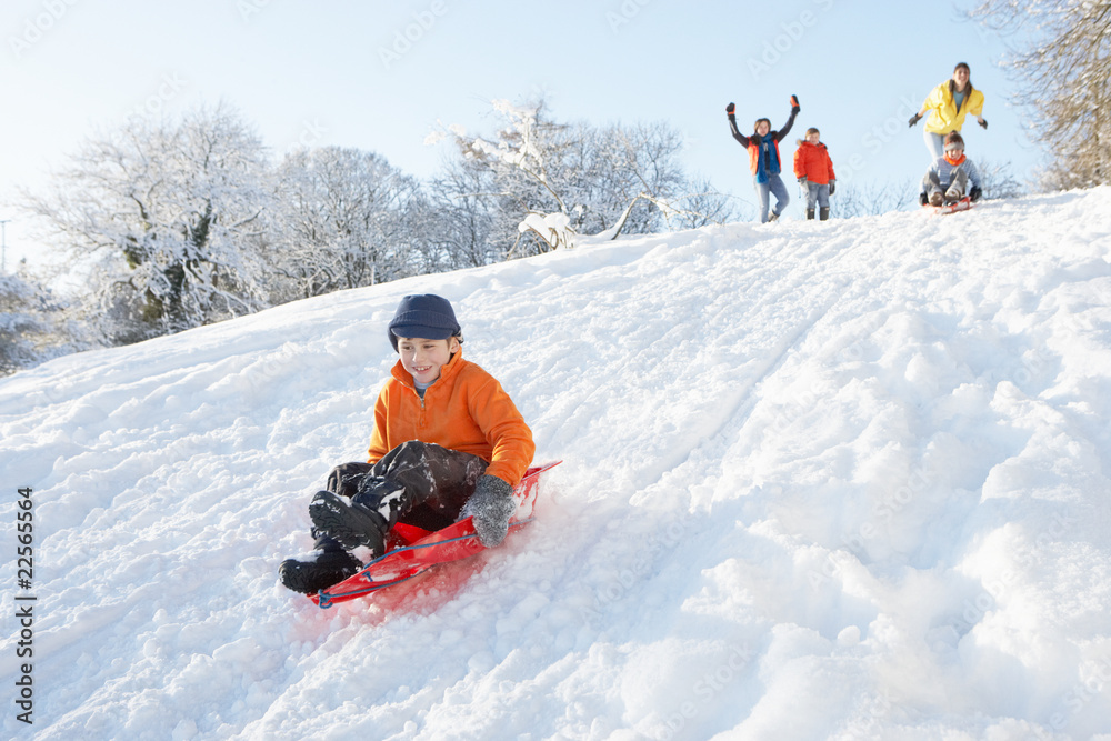 Young Boy Sledging Down Hill With Family Watching