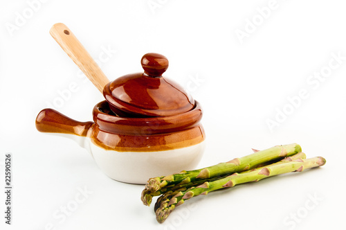 Fotografie Brown soup crock with wooden spoon and fresh green asparagus