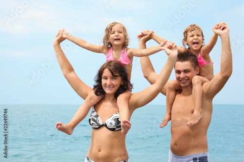 parents near water with little girls sitting on necks handies