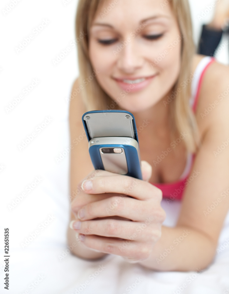 Blond woman sending a text lying on a bed Blond woman sending a text lying on a bed
