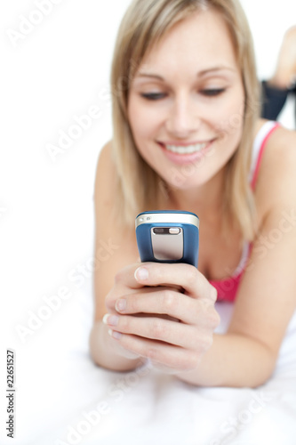 Young woman sending a text lying on a bed