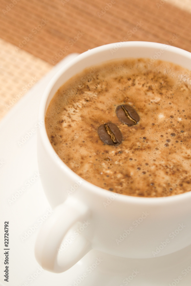 White coffee cup on saucer with two beans floating on surface White coffee cup on saucer with two beans floating on surface