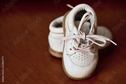 pair of white leather baby shoes with brown wood background