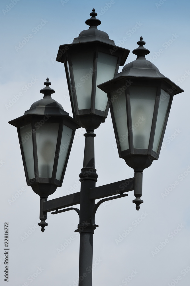 three lanterns on a post on a background sky