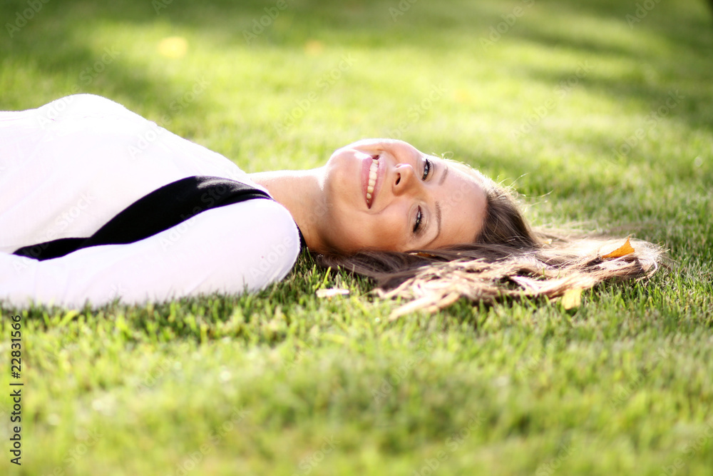Cute young female lying on grass field at the park .