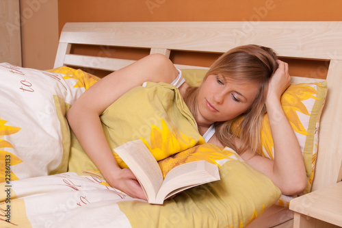 Young blond woman reading book in bed