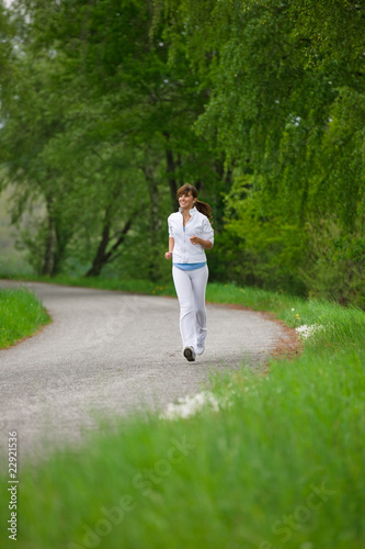 Jogging - sportive woman running on road in nature