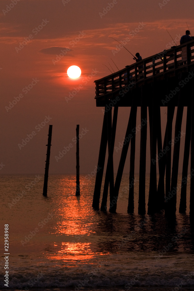 Silhouette of a boy fishing from a pier at sunrise